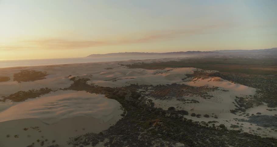 Aerial view of sand dunes near ocean at sunset