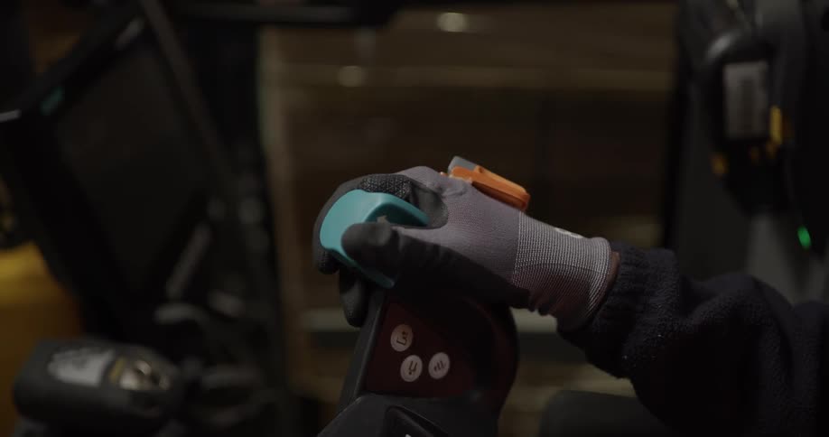 The hand of a worker is seen holding the steering controls ofa forklift in a warehouse