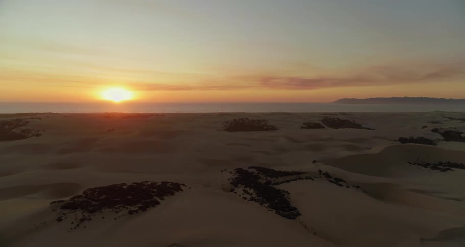 A sandy beach with the ocean and a sunset in the background