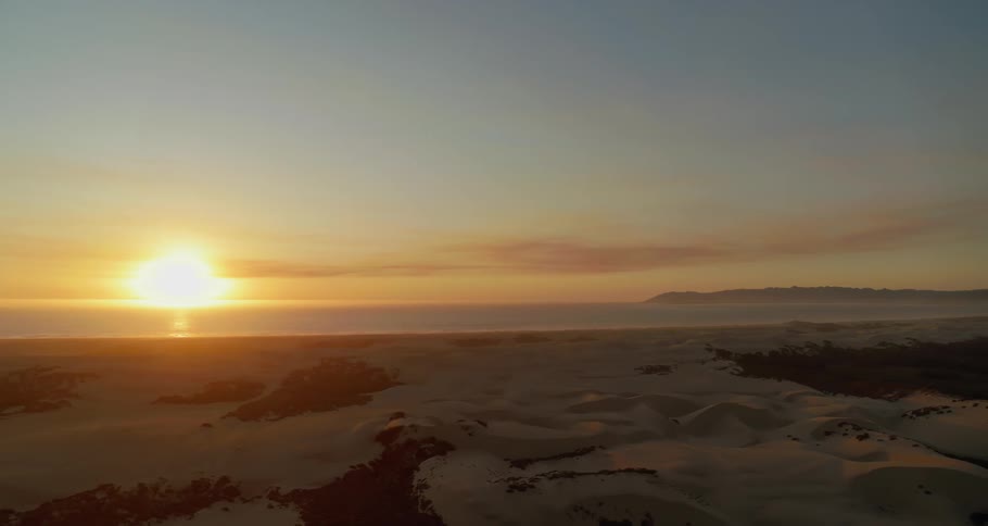 A sandy beach with the ocean and the sunset in the background