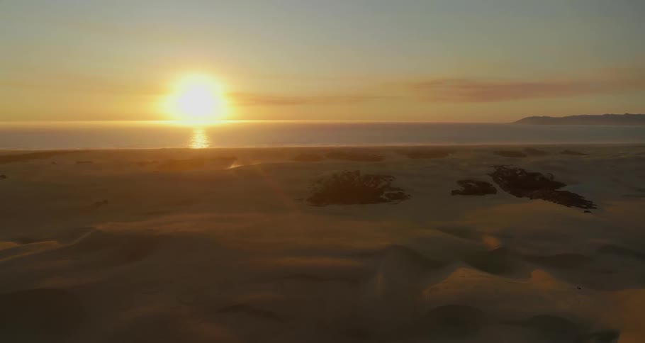 Aerial view of coastal area with sand dunes and calm sea at sunset