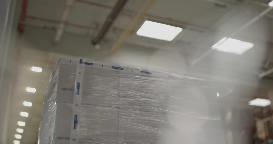 Cardboard boxes wrapped in plastic rotate in a lit bright warehouse