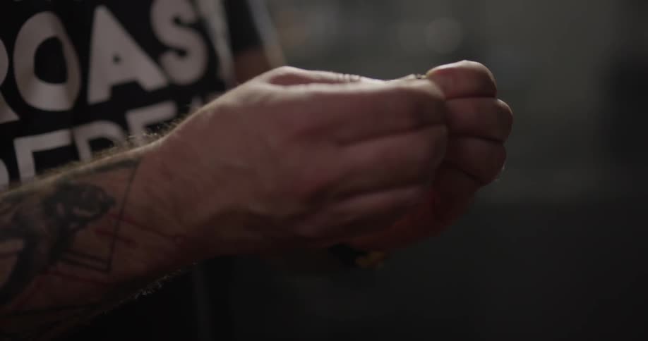 A tattooed man examining and tasting coffee beans