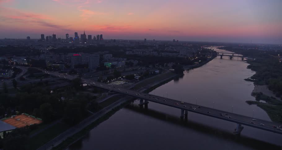 The cars travel on the bridge near the city at dawn