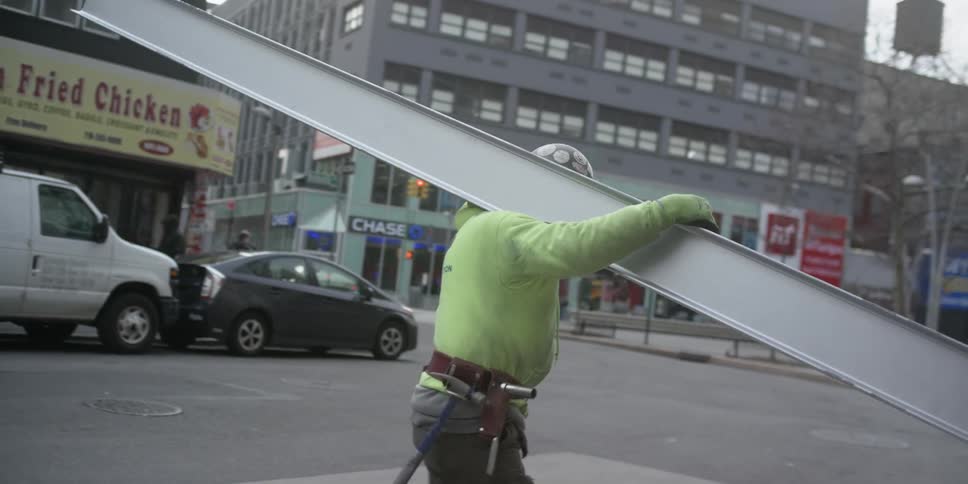 A man is carrying a large metal beam as he crosses the street