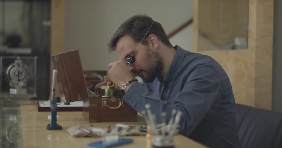 A man uses an ocular magnifying glass to work on something closely
