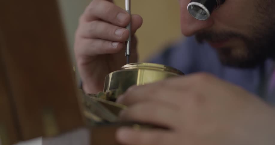 A man wearing a watchmakers loupe uses a screwdriver to repair a clock