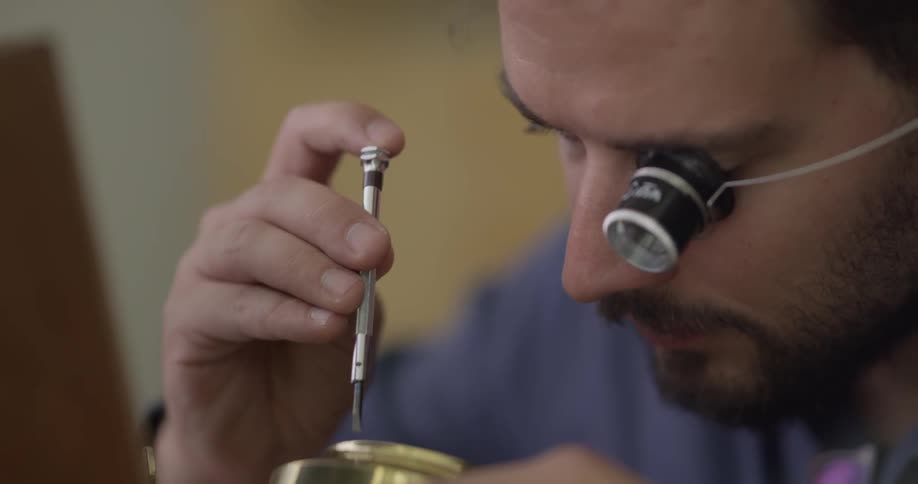 A man wearing a loupe using a screwdriver to unscrew something with one hand