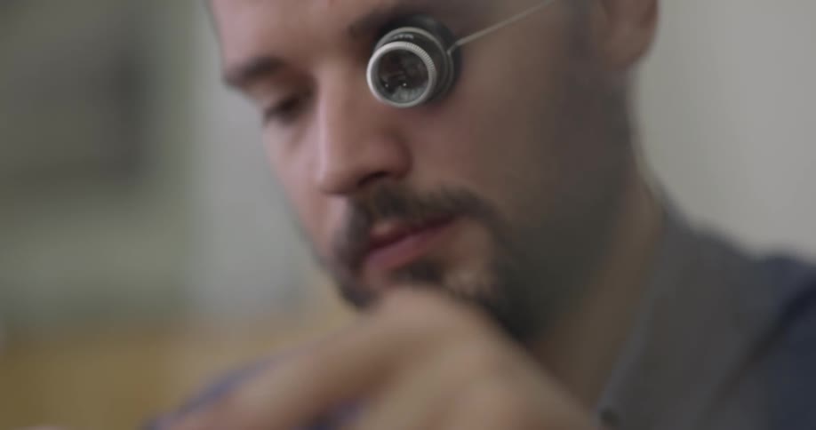 A man with a magnifying glass on his eye fixes a small object