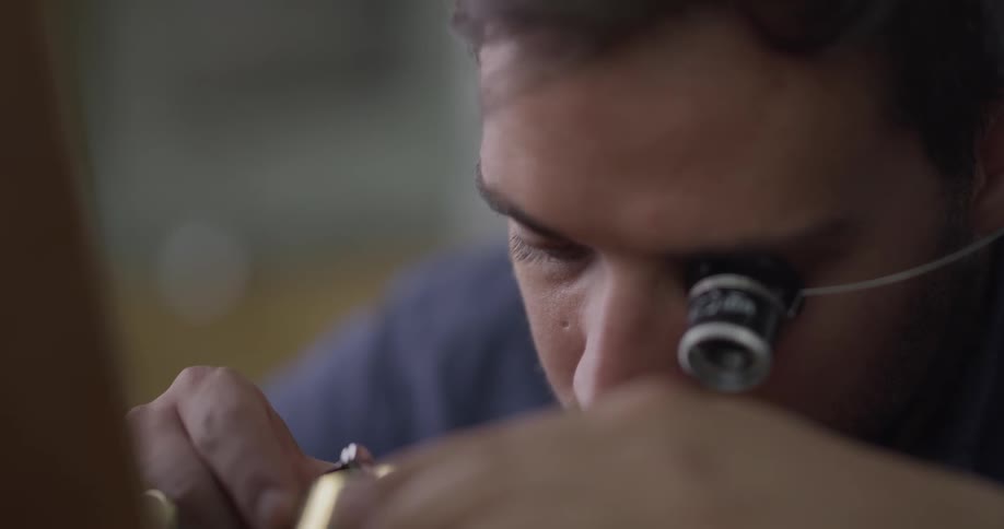 A young man with a magnifying glass on his eye works on a compass