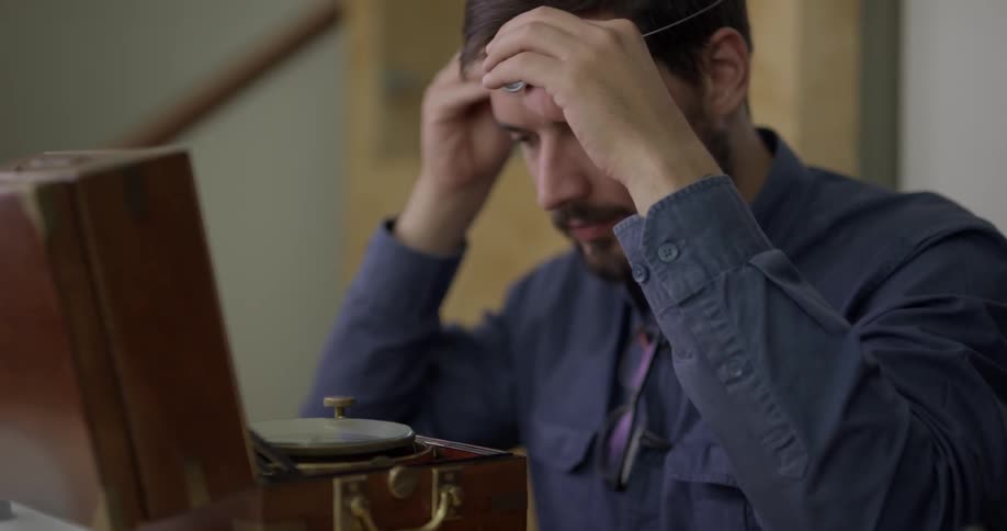 Man wearing jeweler loupe opens small antique box