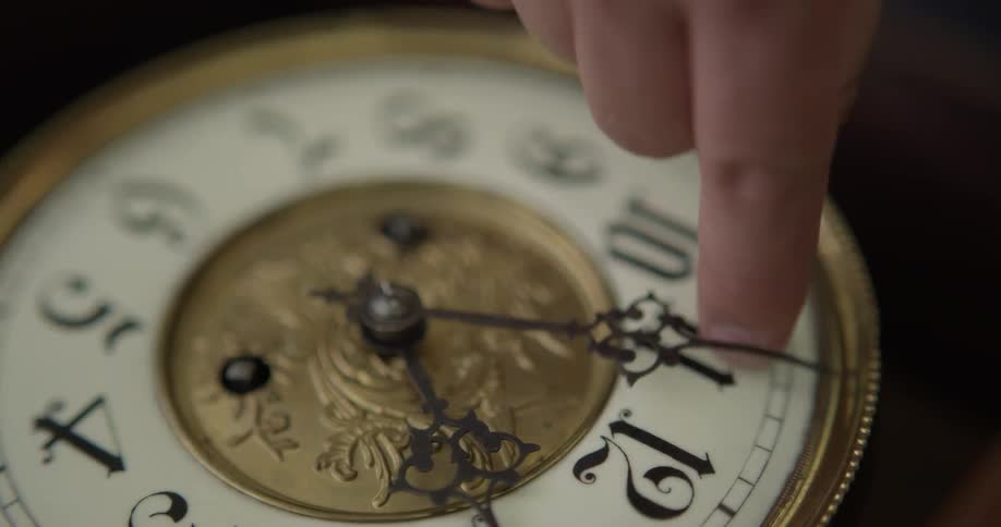 A person turns a hand on an ornate analogue clock to twelve