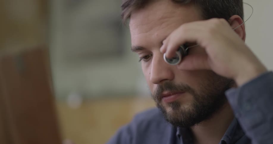 A young man with a magnifying glass over his eye examines an object