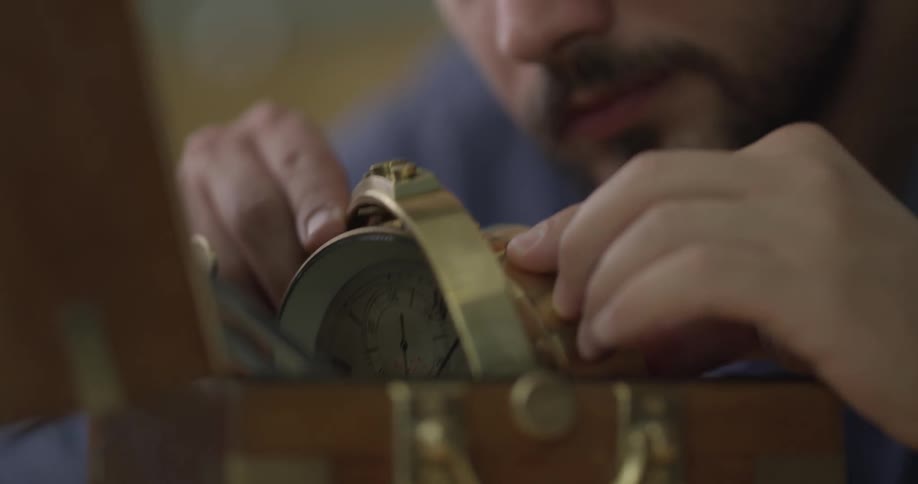 A young man with a magnifying glass on his eye fixes a clock
