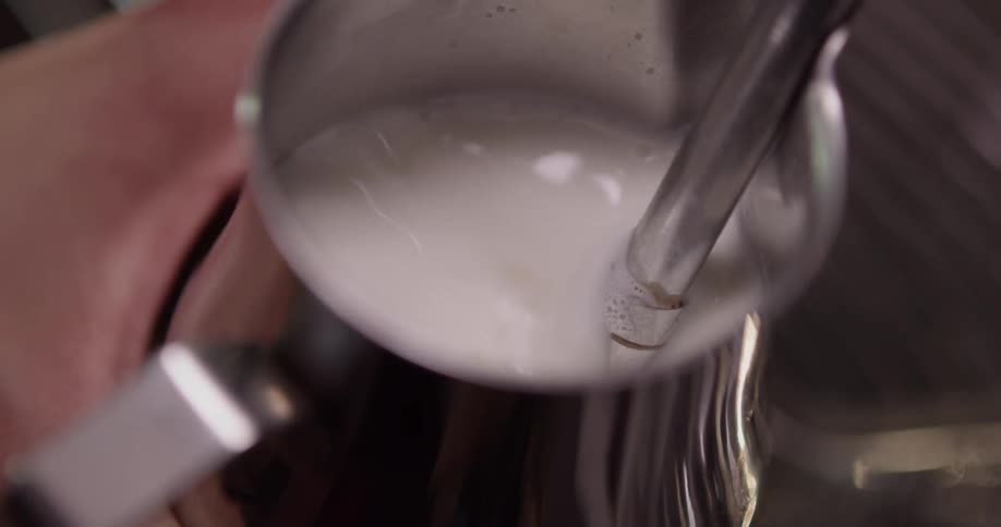 A person lifts a cup under a nozzle to steam milk