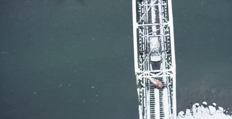 A train is traveling over a bridge as it snows