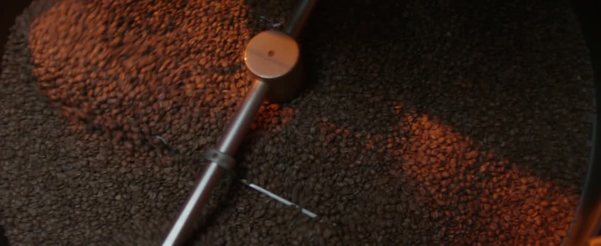 An overhead view of industrial equipment stirring a vat of coffee beans