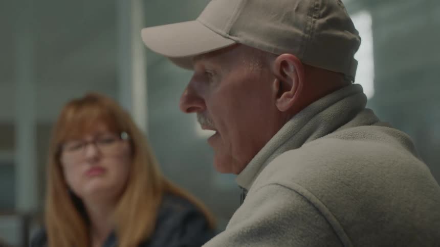 Man wearing cap talk to people sitting at the table during daylight