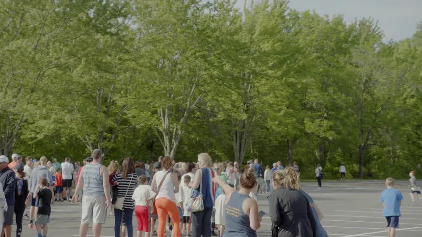 A large group of people are standing in a parking lot and many of them are wearing running apparel and racing bibs