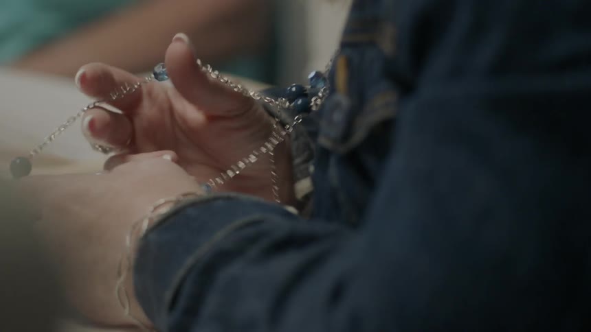 A woman fiddling with her necklace while sitting at a table
