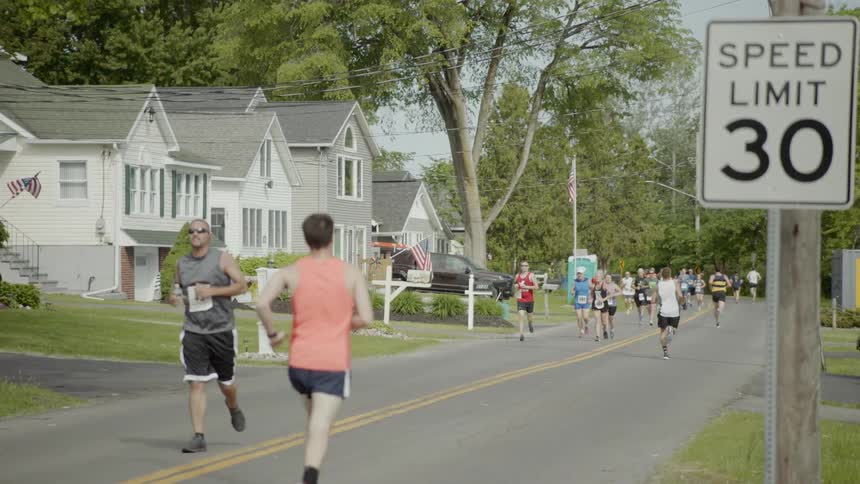 People participate in a road race jogging in both directions on a small town road on a sunny day