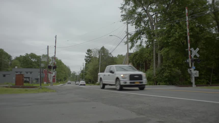 Cars and trucks travel on a rural road over railroad tracks at a crossing