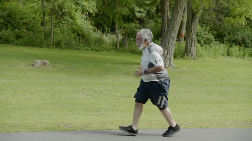 An elderly man with a running bib on runs along the side of the road