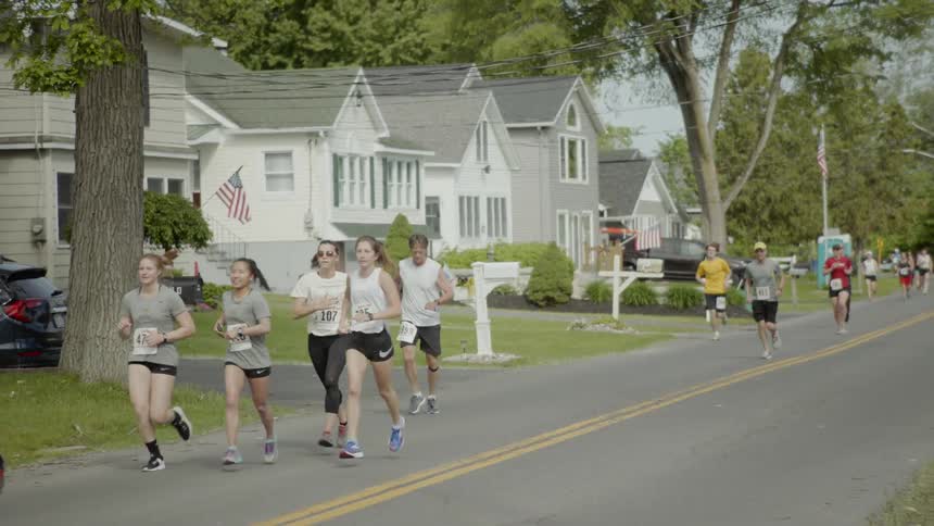 People wearing numbers run past homes and lawns as they participate in a road race
