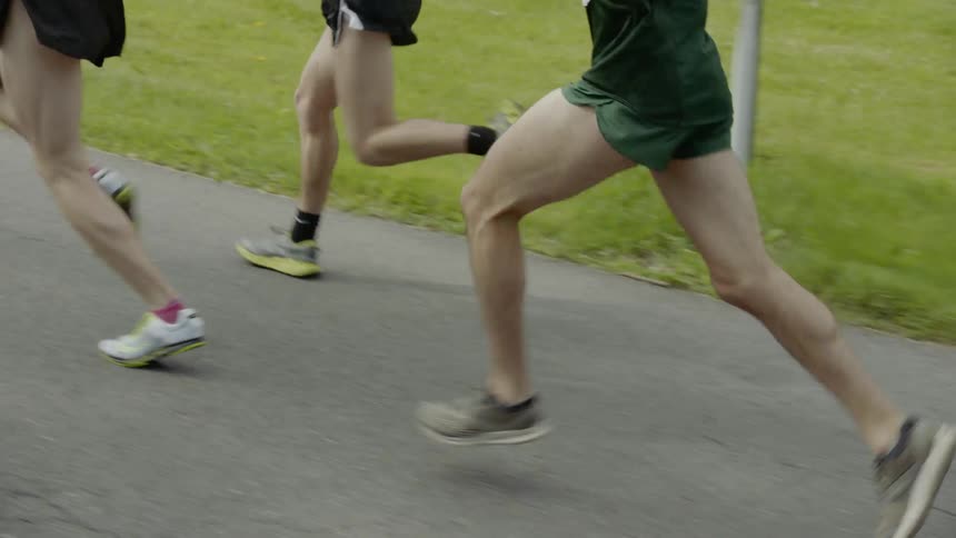 A small group of men wearing racing numbers run on a road past homes and lawns