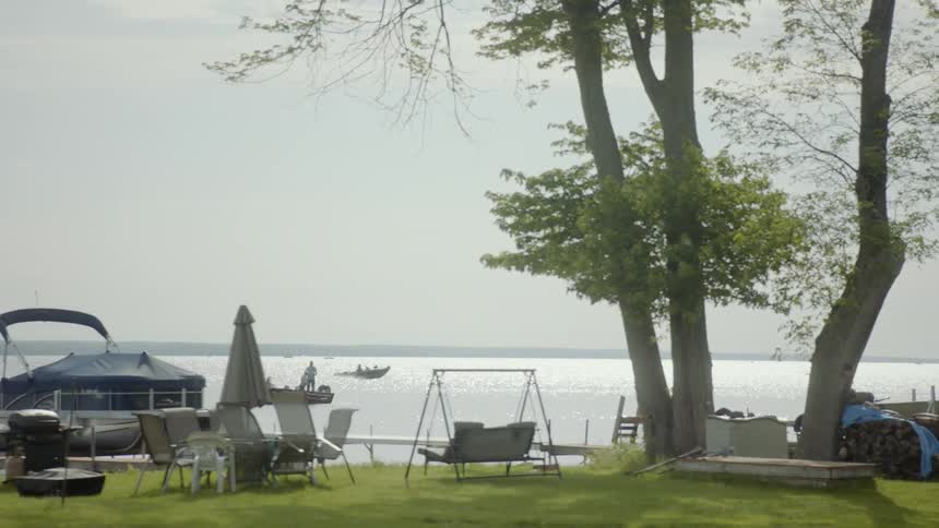 Chairs and grills line the grassy shore where boats are anchored while others travel by