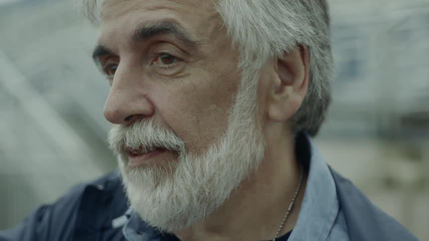 Bearded grey hair man smiles and looks around during daylight