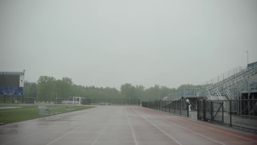 Rain falls on an outdoor running track on a cloudy summer day