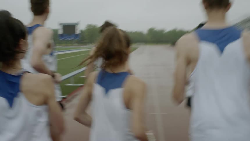 A group of young male and female runners on a school team are all running together around an outdoor track