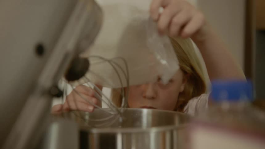 A girl shaking the last remnants of batter from a plastic bag into a pot
