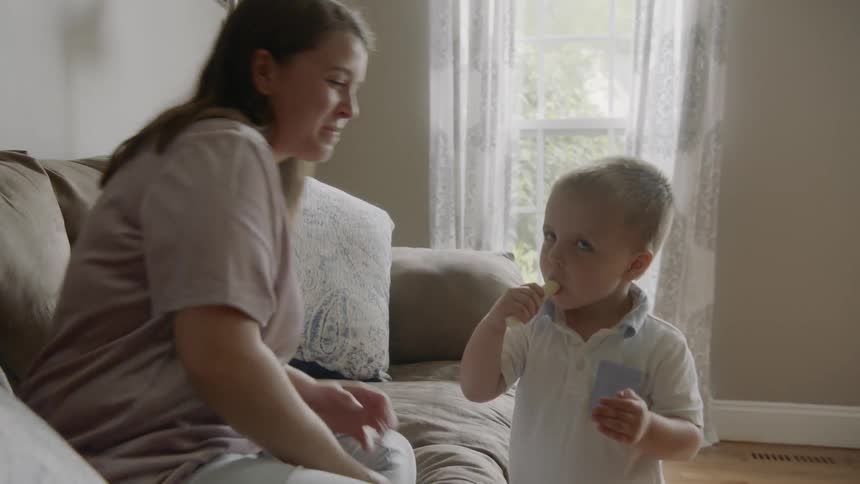 Woman sitting on the couch plays with toddler boy at home