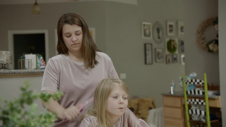 A woman is brushing a girls hair