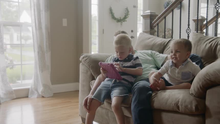 A man sits on the couch with his boys as one play with an electronic device
