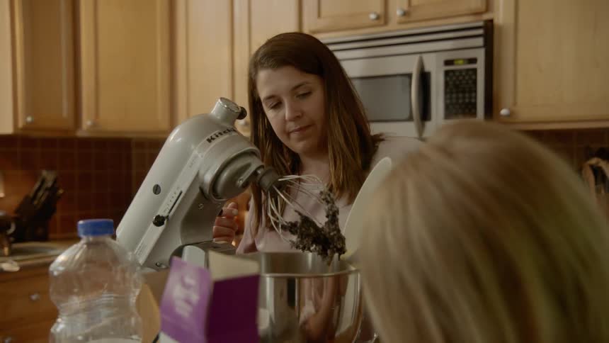 Mother and daughter pouring ingredient from a white bowl into mixer