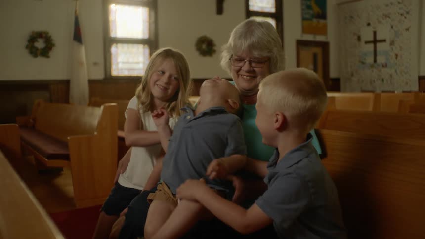 An older woman plays with three children in a church pew