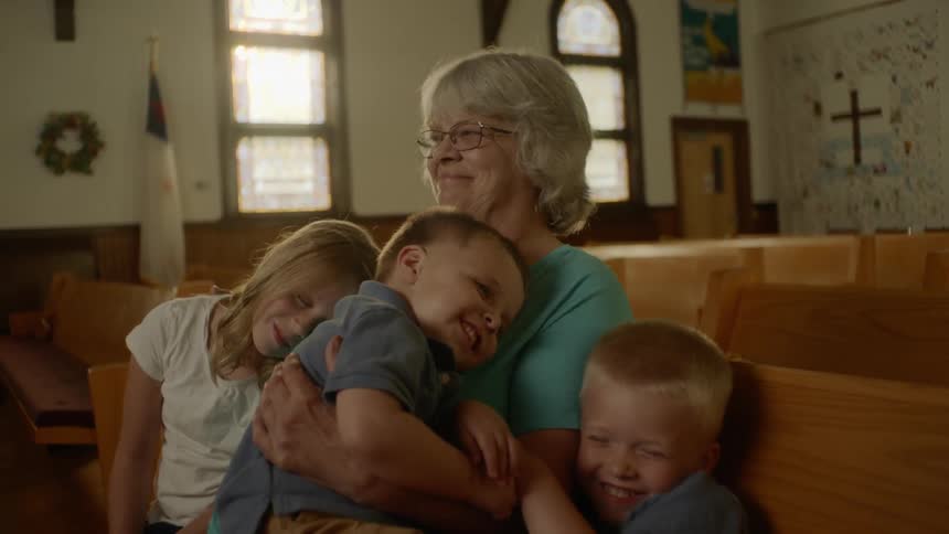 An old woman sitting on a pew in a church while hugging three young children