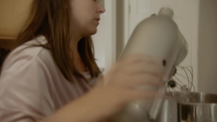 A woman puts a bowl in the microwave then talks to a little girl and gets something out of the fridge