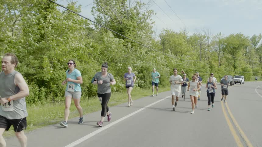 A group of marathon runners racing down a road through a woodland