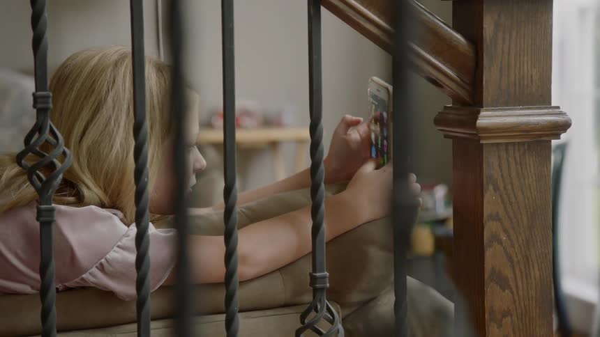 A little girl lies on a sofa and plays with a cell phone