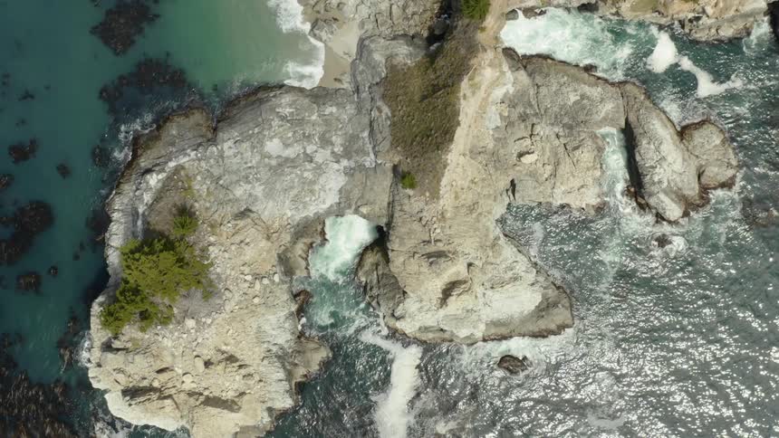 A rocky prominence protrudes out from the shoreline into the ocean as the waves continue to crash into its rocky shores