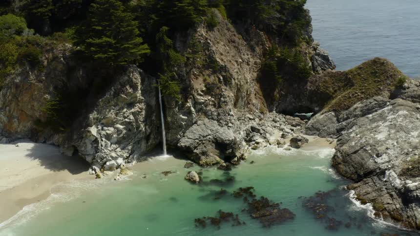 Water pours out of a coast side mountain cliff into the ocean below