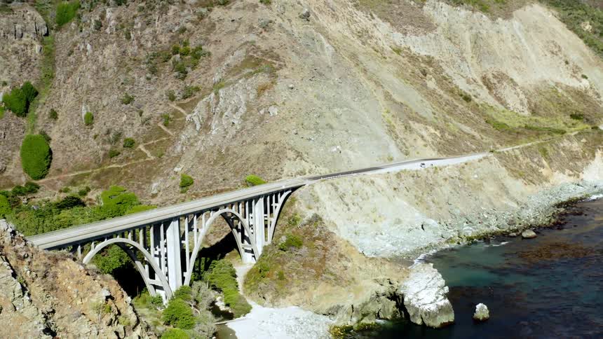 An aerial view of a shoreline and bridge between mountains