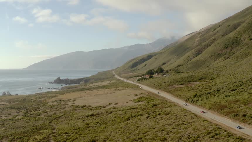 The vehicles drive one behind the other on the road by the hill