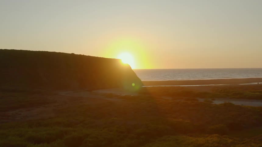 The sun rising over the ocean partially hidden by cliffs