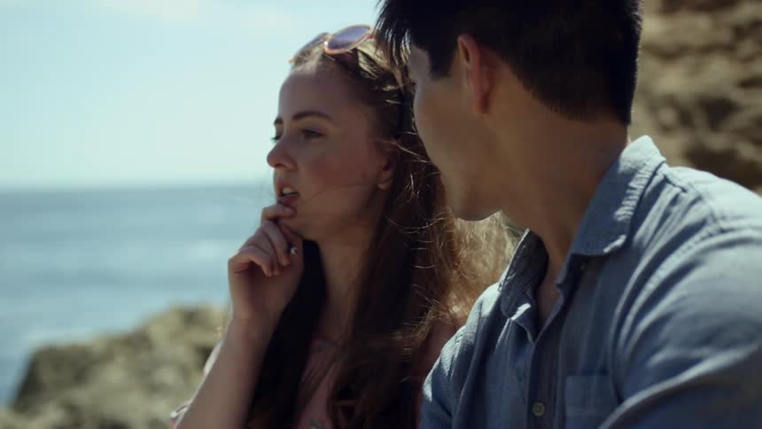 A man and a woman talking while standing on rocks next to the ocean