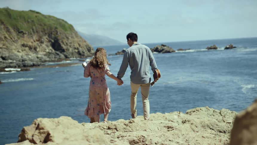 A couple climb over the rocks towards the water
